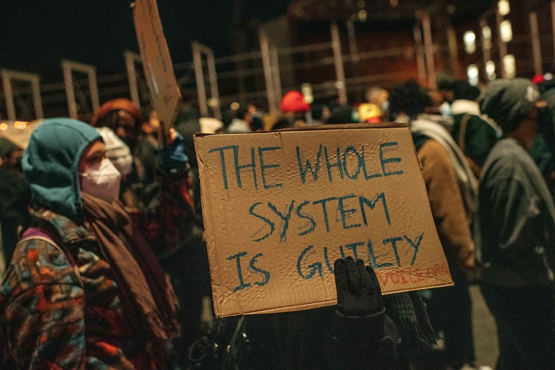 A protester holds up a sign reading, "The whole system is guilty" during a demonstration against the not guilty verdict for Kyle Rittenhouse on November 19th.